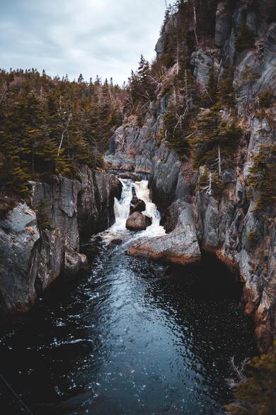 River Near Rocky Terrain Under Gray Sky