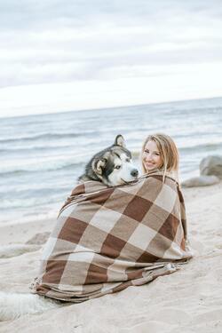 Girl and Dog Sitting Together in Blanket on Beach