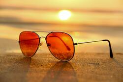 Red Lens Sunglasses on Sand Near Sea at Sunset Selective Focus Photography